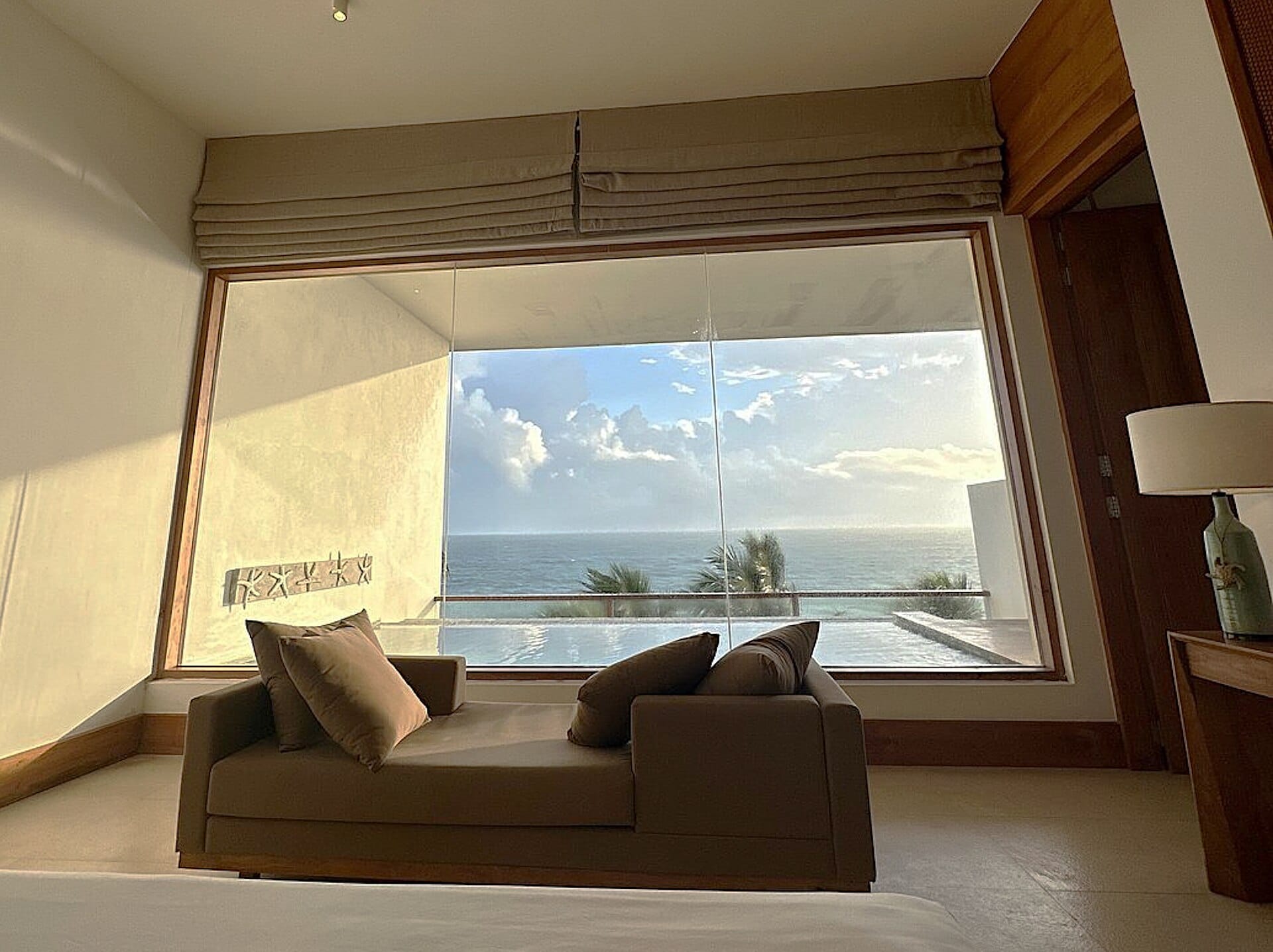 Habitació d'hotel d'alta gamma amb un sofà davant d'un gran finestral amb vistes al mar i estors de tela.