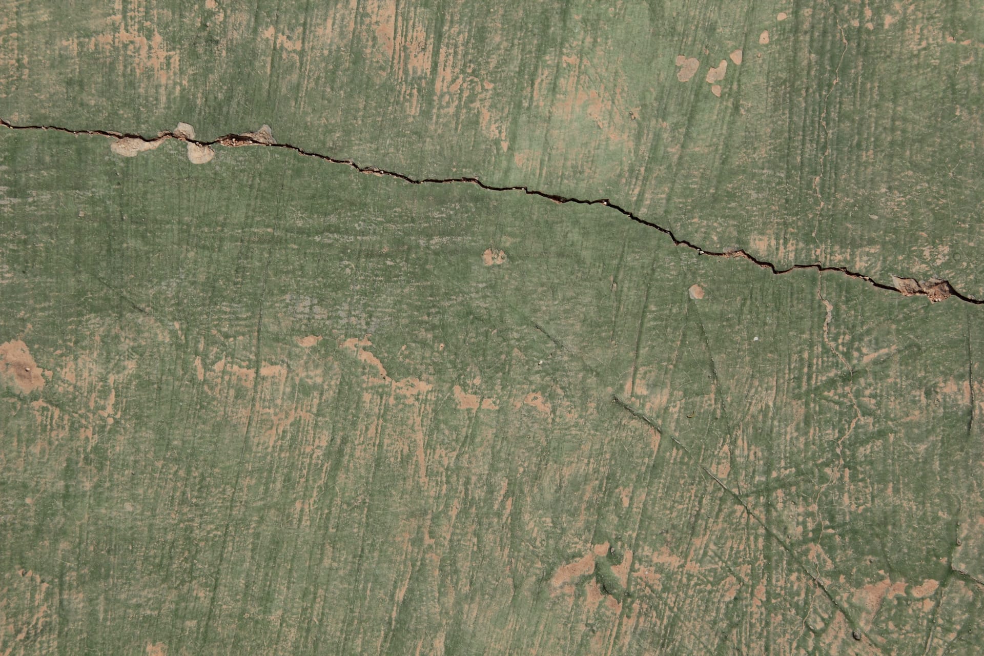 Close-up of a crack running across a green-painted rendered wall with flaking paint.