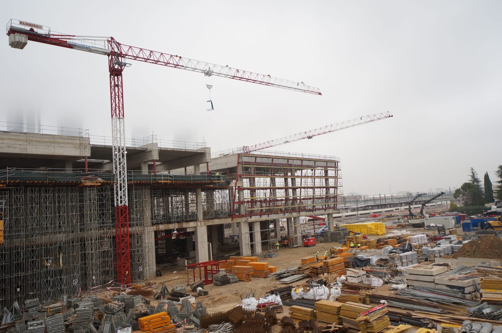 Concrete building under construction with tower cranes and stacked building materials.