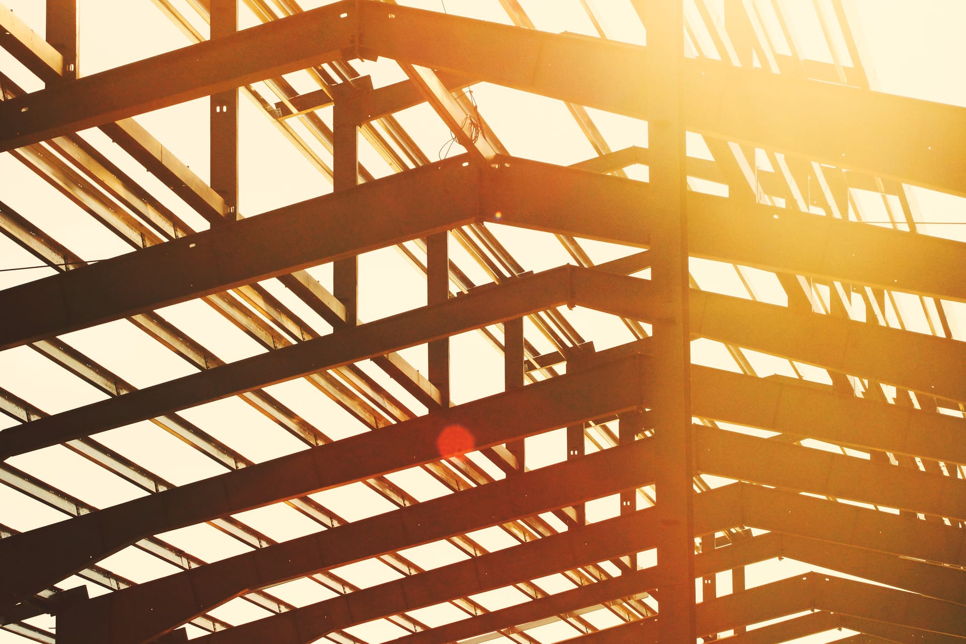 Steel beam and column frame of a building under construction, backlit by the sun.