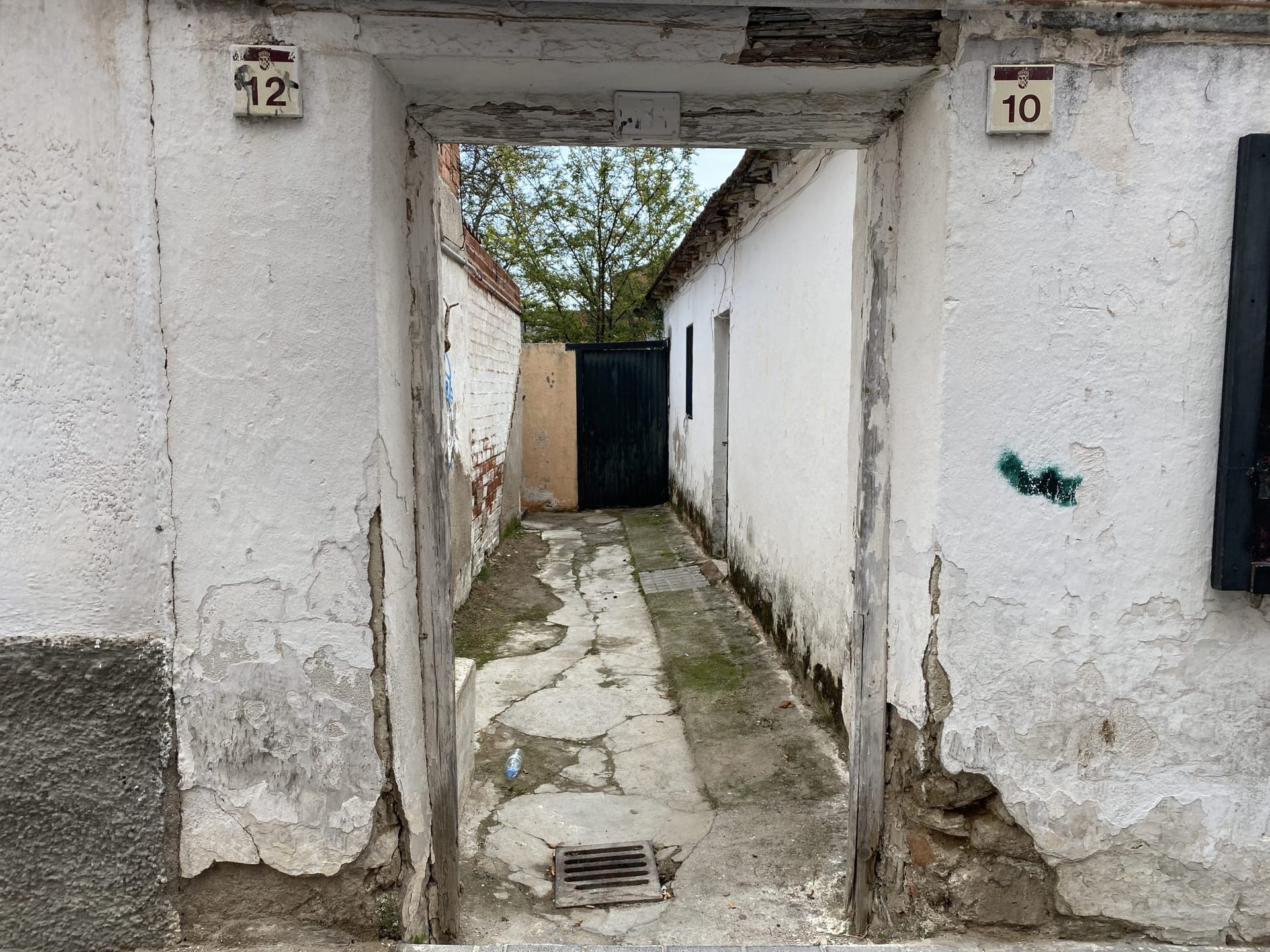 Paso estrecho entre dos edificaciones encaladas con el revoco desconchado y manchas de humedad en la parte baja de los muros.