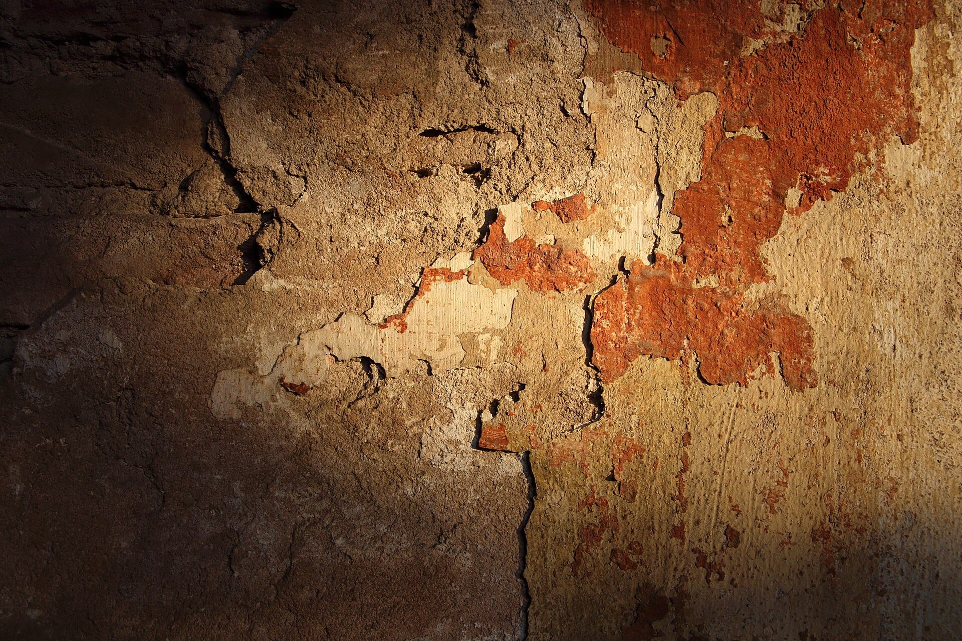 Detalle de un muro antiguo con el enlucido degradado, manchas de humedad y fisuras.