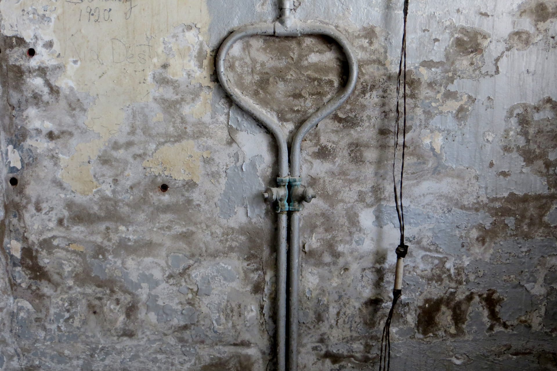 Interior wall with flaking plaster and damp stains around a pipe.