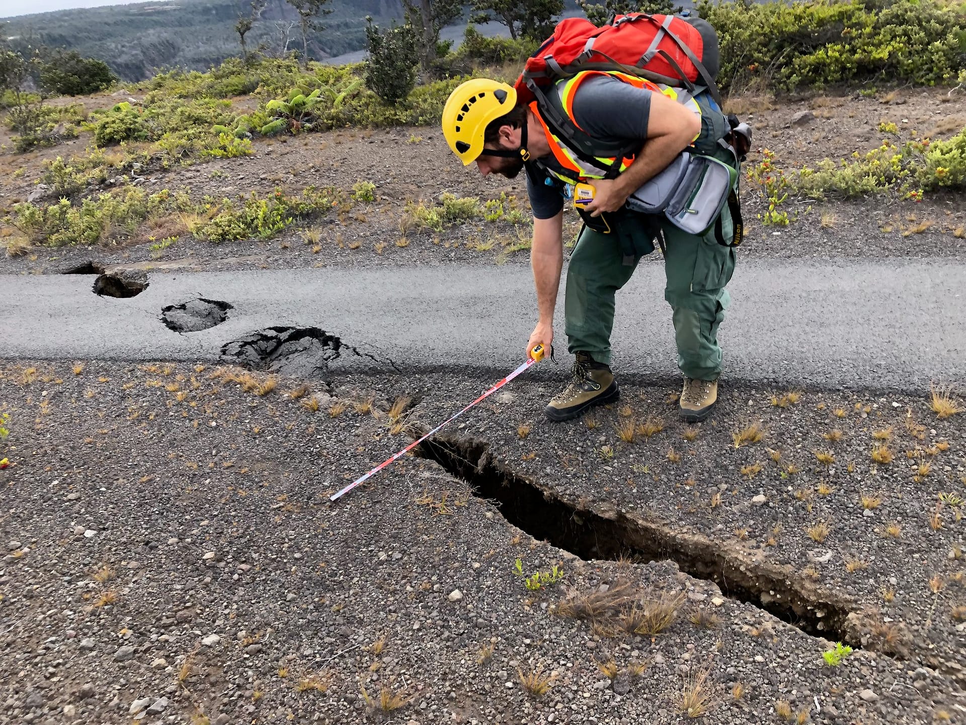 Técnico midiendo con una cinta una grieta abierta y varios hundimientos en el borde de una carretera asfaltada.