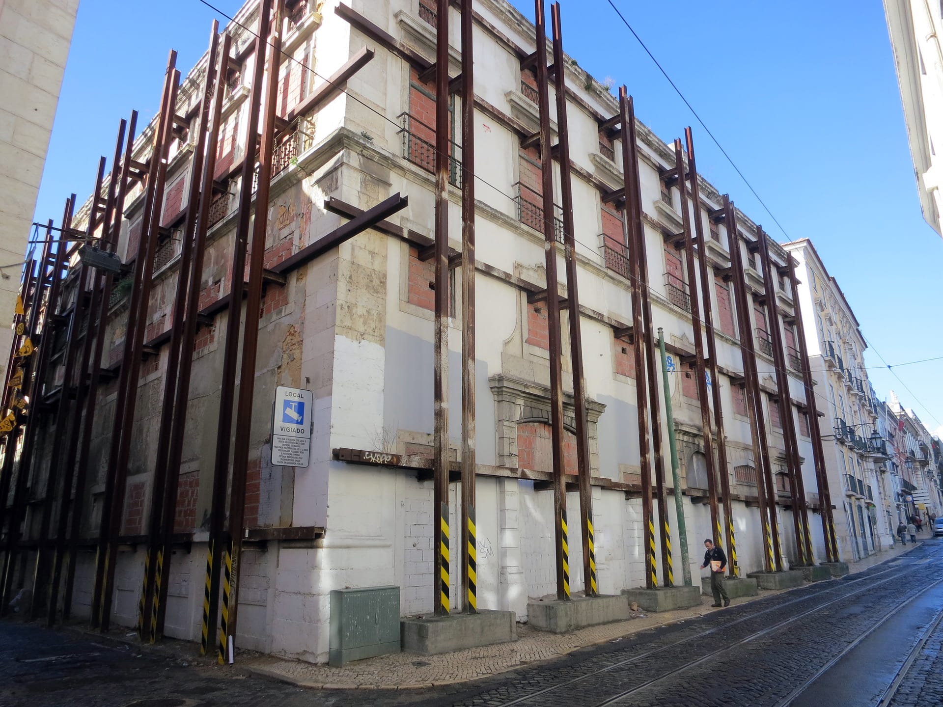 Fachada de un edificio antiguo en una calle empedrada, apuntalada con perfiles metálicos y con los huecos tapiados.